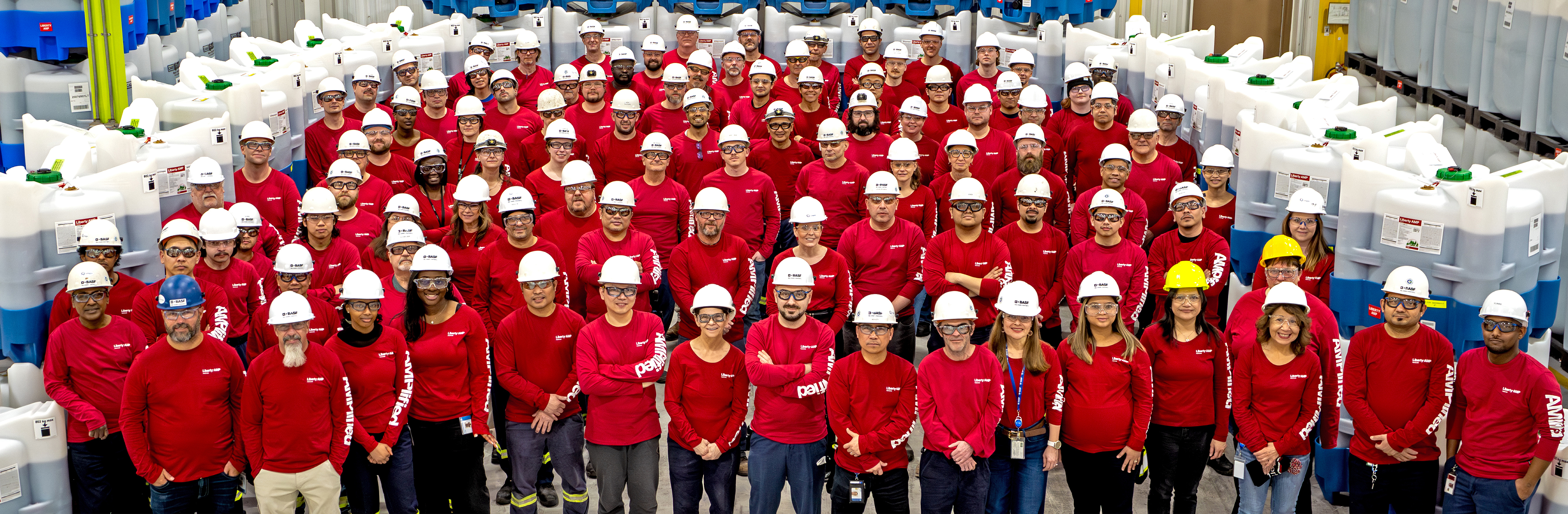 Large group of individuals smiling and wearing hard hats in facility
