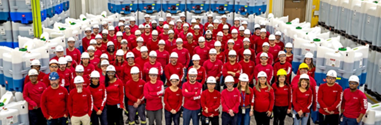 Large group of individuals smiling and wearing hard hats in facility