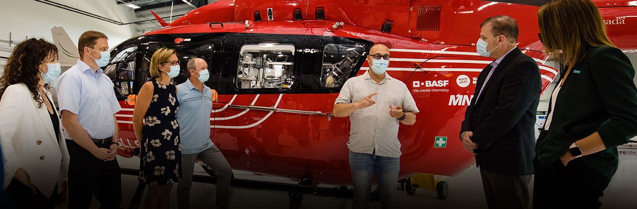 Man speaking to group of people with a helicopter in the background