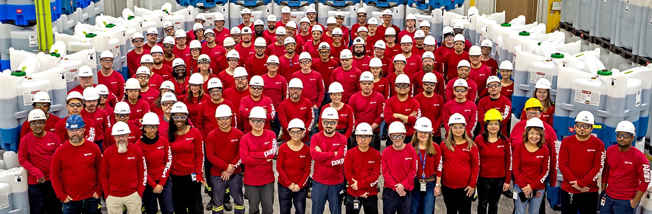 Large group of individuals smiling and wearing hard hats in facility